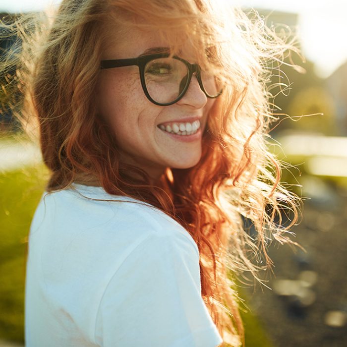 Portraits of a charming red-haired girl with a cute face. Girl posing for the camera in the city center. She has a wonderful mood and a lovely smile.